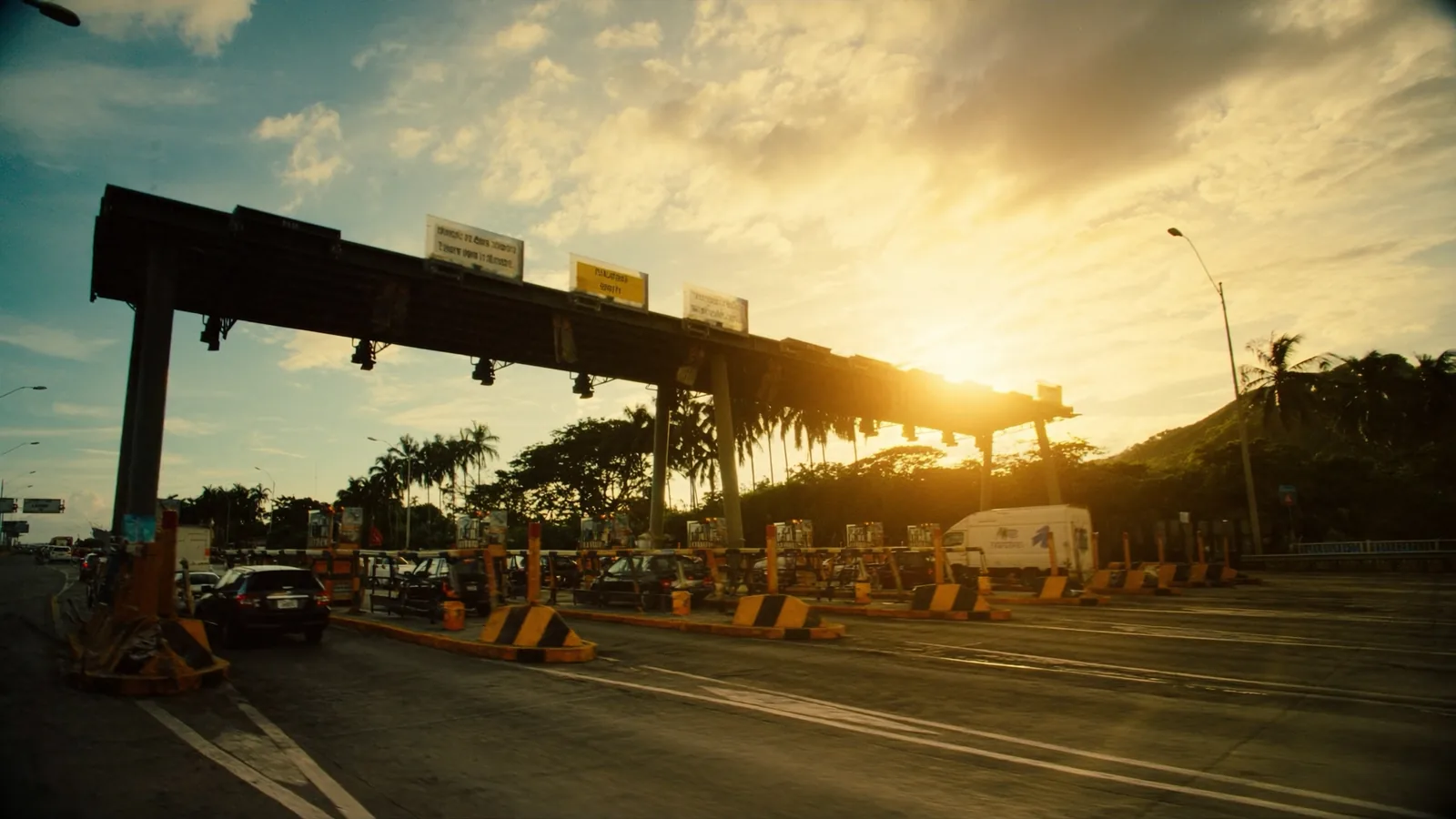Vehicles passing through electronic toll lanes at a Philippine expressway plaza at sunset