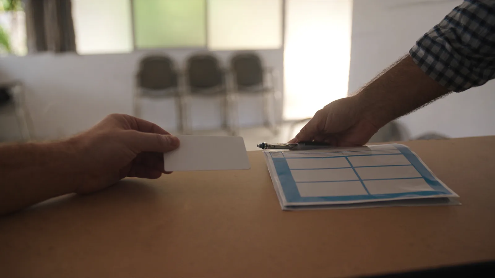 Hands holding vehicle registration papers and an identification card across a service counter