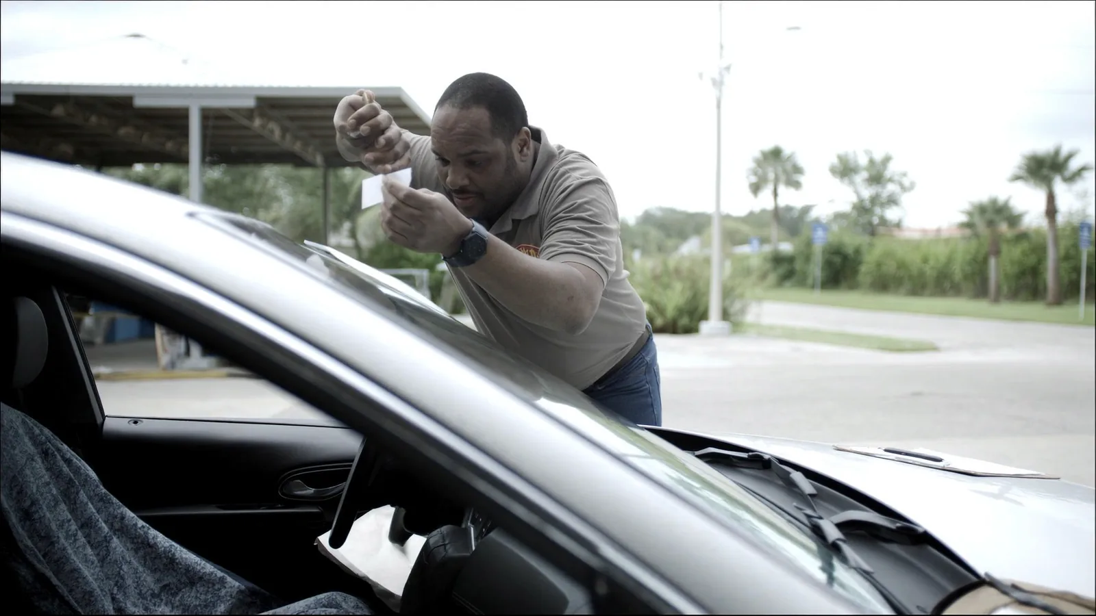 A technician fitting an electronic toll tag to the inside of a car windscreen at an outdoor service bay